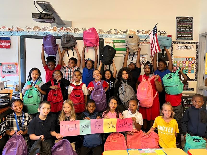 Students holding up donated backpacks with a thank-you sign